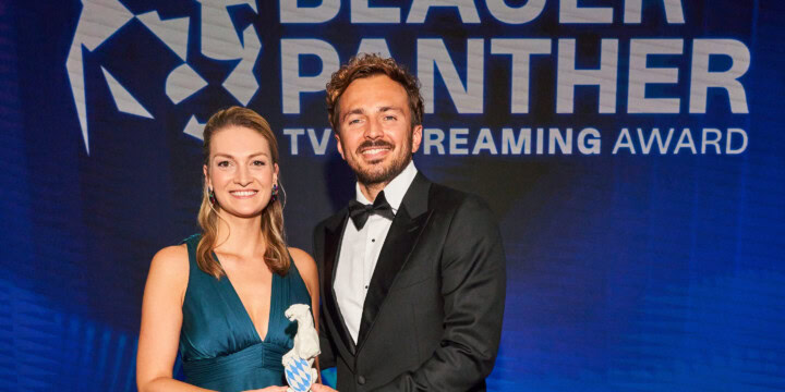 Judith Gerlach und David Helmut bei der Preisverleihung des Blauen Panthers 2022. Beide haben die Hand an der Panther Statue.