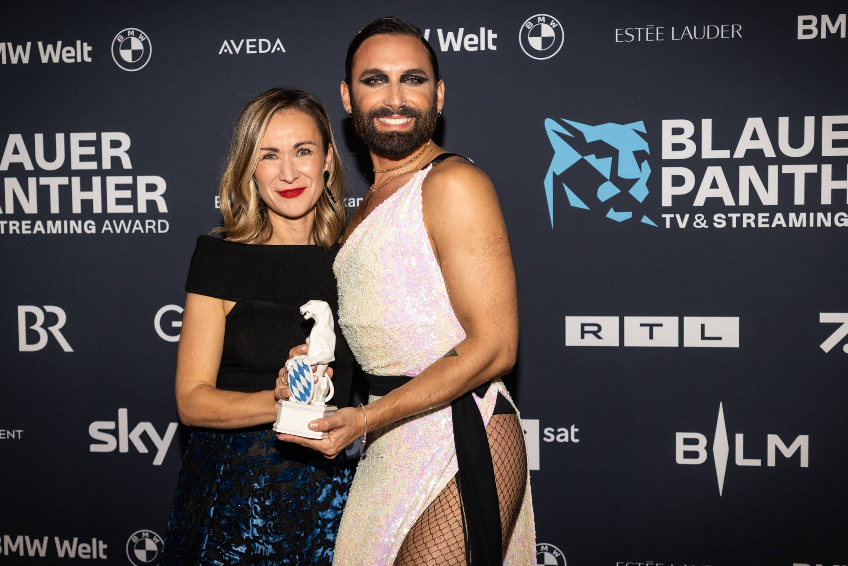 Producerin Anna-Lena Zwez und Conchita Wurst vor der Pressewand bei der Preisverleihung 2022. Beide die Hand an der Panther Statue.