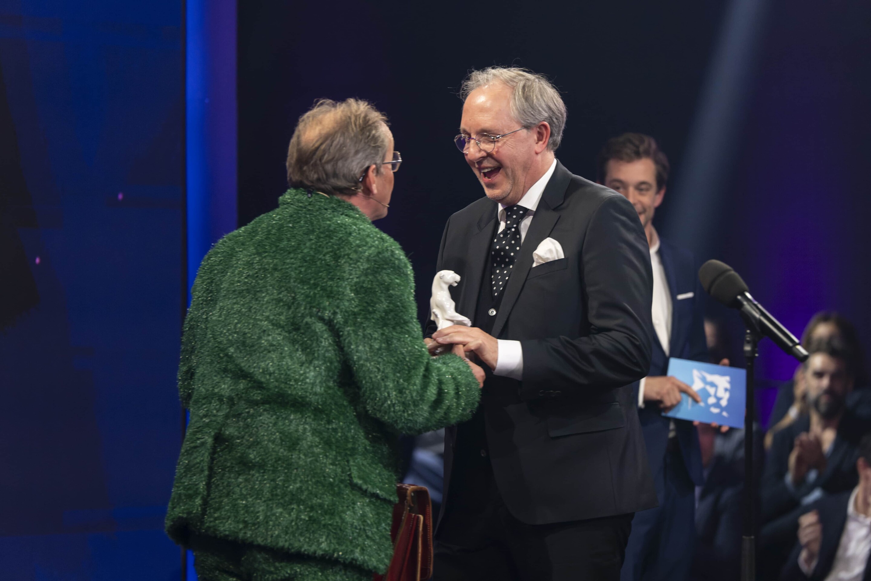 Two men in suits shaking hands at a awards ceremony