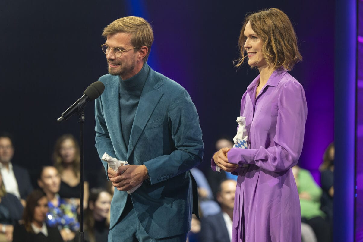 Joko Winterscheidt und Julia Mehnert (c) Medien.Bayern _ Ralf Wilschewski (1) Executive Producer Julia Mehnert (rechts) und Moderator Joko Winterscheidt (links) bei der Preisverleihung. Joko steht am Mikrofon und hält eine Dankesrede.
