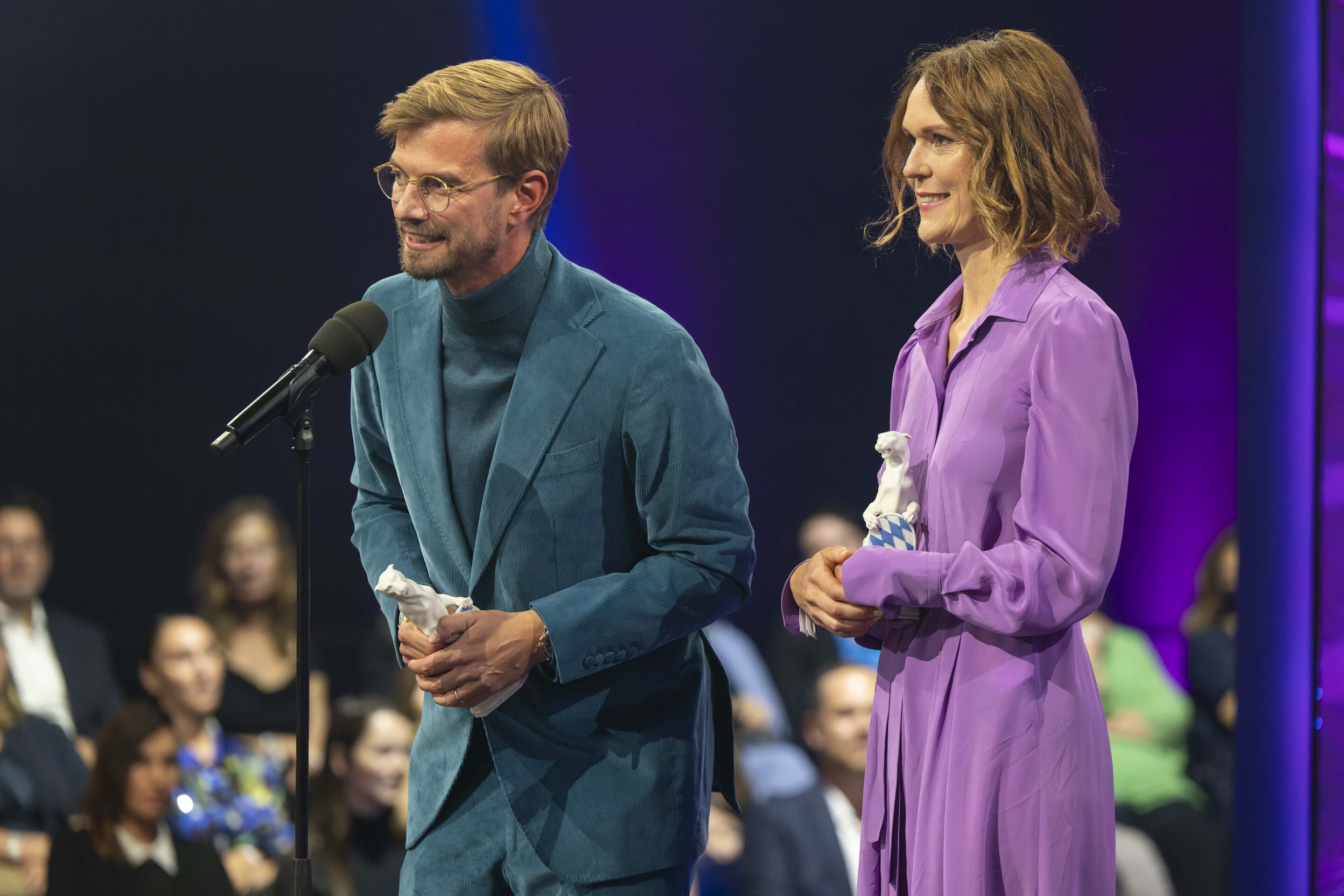 Executive Producer Julia Mehnert (rechts) und Moderator Joko Winterscheidt (links) bei der Preisverleihung. Joko steht am Mikrofon und hält eine Dankesrede.