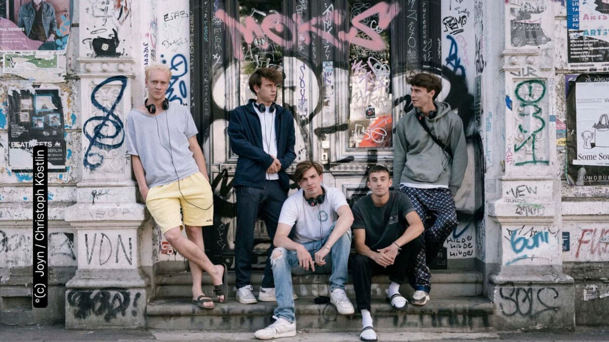 BP 23 „Intimate“ 08 (c) Joyn Christoph Köstlin Emil Belton, Oskar Belton, Max Mattis und Leo Fuchs stehen und sitzen vor einer mit Graffitti besprühten Wand (c) Joyn Christoph Köstlin