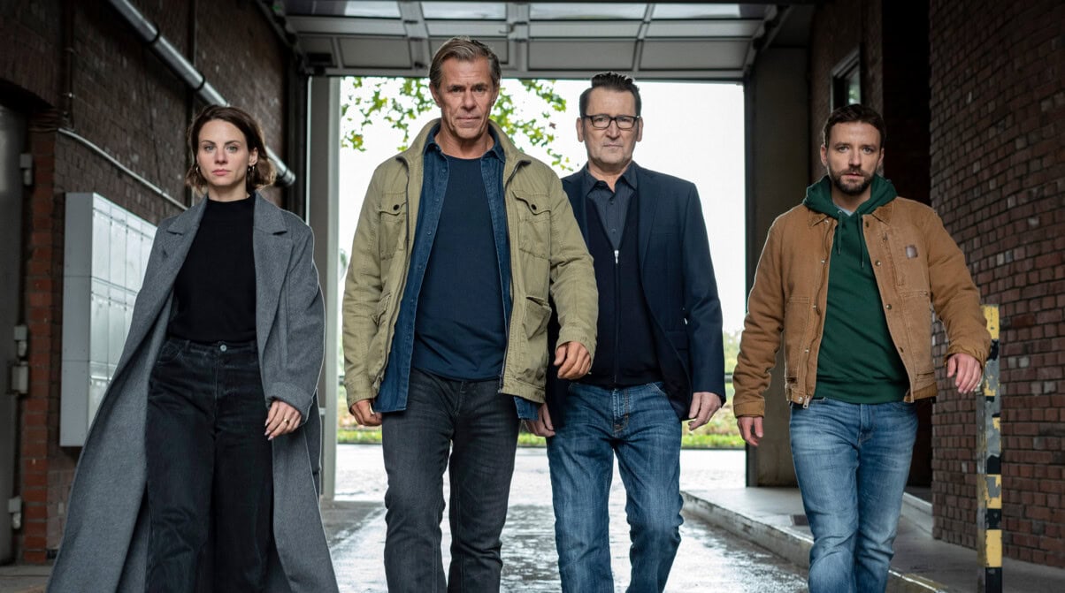 Morden im Norden - ARD Vier Personen laufen der Kamera entgegen und schauen in die Kameralinse. Es sind drei Männer und eine Frau. Sie wirken selbstbewusst. Sie befinden sich in einer großen Halle oder Scheune.