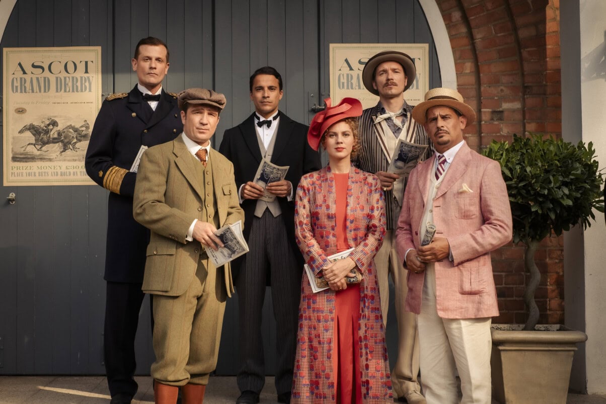 Miss_Sophie_c_Gordon_Muehle_Amazon MGM Studios TV & Streaming Tipps Dezember 2025: Sechs Personen in eleganter Kleidung der 1920er Jahre posieren vor einem Eingang mit „Ascot Grand Derby“-Plakaten und halten Rennprogramme in den Händen.