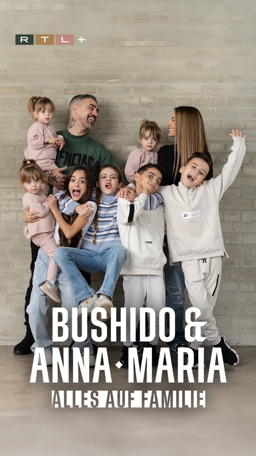 Bushido_9zu16 TV & Streaming Tipps im August – Special „Beliebteste Reality-Serie” Plakat zur Serie ‚Bushido & Anna-Maria – Alles auf Familie‘ bei RTL+. Darauf sind Bushido, Anna-Maria und ihre Kinder zu sehen. Sie lachen, kuscheln und stehen eng zusammen vor einer grauen Wand. Unten steht der Serientitel groß in weißer Schrift.