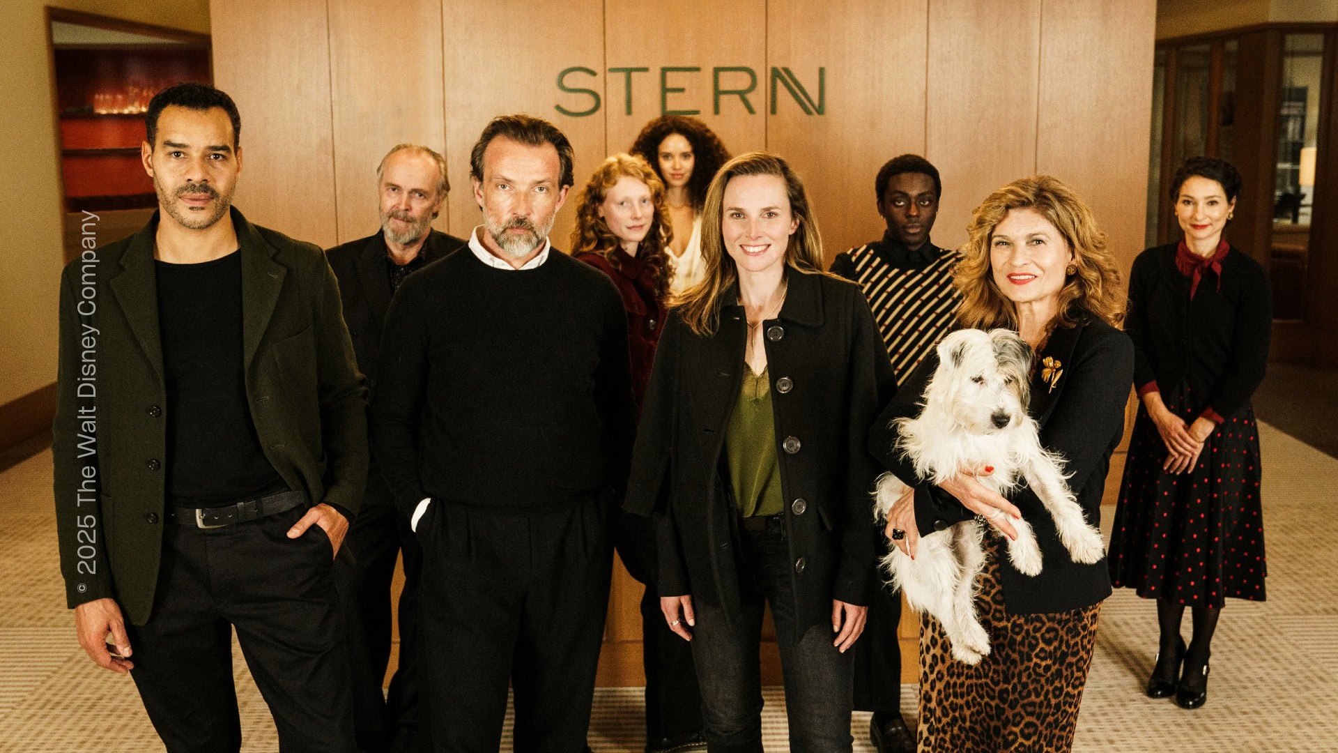 Mehrere Personen stehen im Foyer eines Büros und blicken direkt in die Kamera, sie tragen lockere Businesskleidung. Eine Person hält einen Hund auf dem Arm.