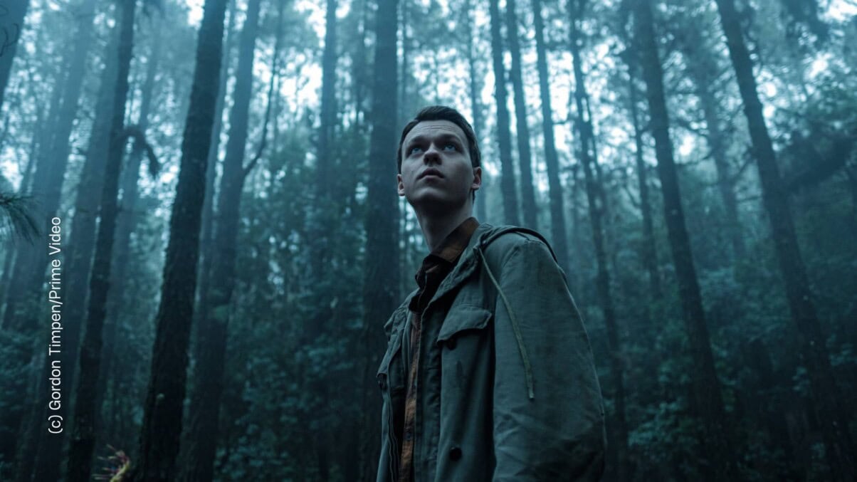 bp-23-hohlbeins-der-greif-3-c-prime-video-mfrh-original-scaled_1 Ein junger Mann steht in einem düsteren Wald und blickt in die Ferne.