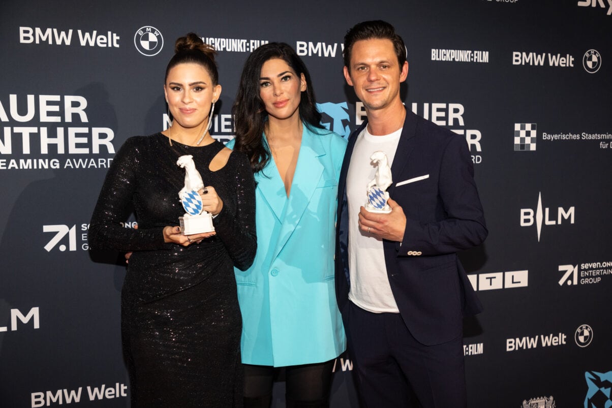 Salwa Houmsi, Laudatorin Samira El Ouassil und Jo Schück (c) Medien.Bayern - Johannes Müller Preisträger:innen Salwa Houmsi (links) und Jo Schück (rechts) mit der Panther Trophäe und in der Mitte Laudatorin Samira el Ouassil
